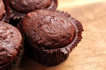 Freshly baked chocolate muffins in brown paper wrappers on a wooden surface