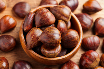 Wooden bowl with fresh harvested chestnuts and scattered organic nuts on rustic table.