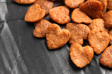 Heart shaped crunchy cat treat pieces scattered on a sleek black textured surface. Dry pet food snacks. Close up