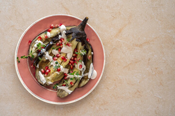 Roasted eggplant with tahini, fresh thyme and pomegranate seeds on ceramic plate over marble Middle East food. Top view.