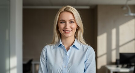 A happy young businesswoman smiling and standing in an office, wearing a blue shirt

