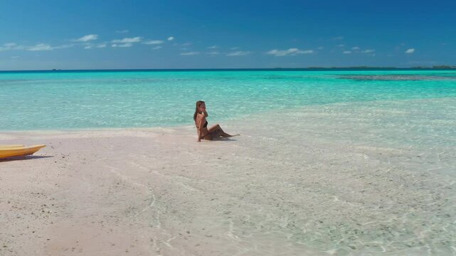 Woman is enjoying the tranquility of a secluded beach, with crystal-clear turquoise water gently lapping at the shore and a kayak resting on the pristine sand