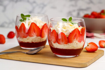 Tasty trifle dessert. Sponge cake, strawberries, jam and whipped cream in glasses on white table, closeup