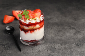 Tasty trifle dessert. Strawberries, sponge cake and whipped cream in glass on grey table, space for text