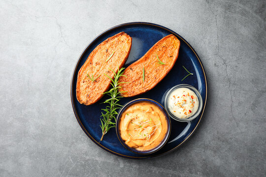 Halves of tasty baked sweet potato served with sauces on grey textured table, top view