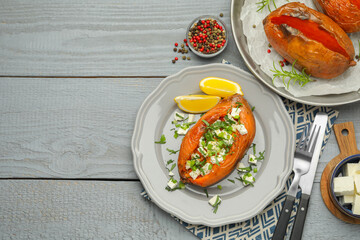 Tasty cooked sweet potatoes served with feta cheese on grey wooden table, top view. Space for text