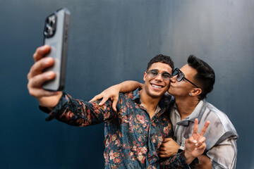 Happy latin gay couple taking a selfie smiling with peace sign
