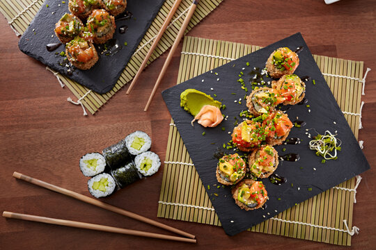 Top view of an assortment of sushi with garnishes on black slate