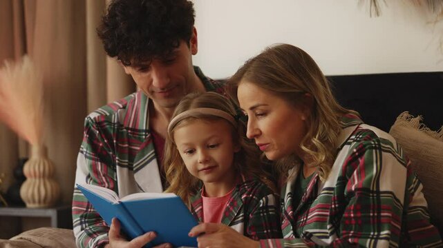 Mom and dad read a storybook to their little daughter while resting in bed