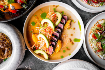 beautifully presented dish featuring seared tuna slices garnished with fresh vegetables, citrus segments, and vibrant sauces, surrounded by an array of colorful appetizers on a stylish table setting.