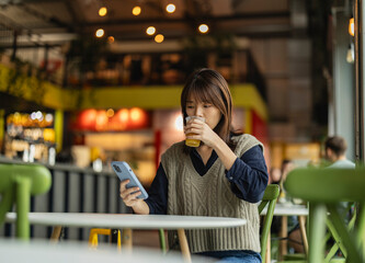 Fototapeta premium Young woman using smartphone and drinking juice in london cafe