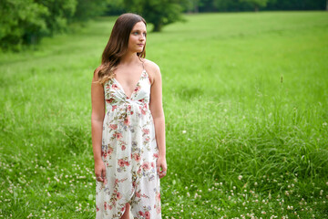 Beautiful young brunette woman in floral print dress stands in field in summer