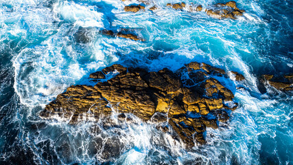 Bare rock sticking out of water. White foamy waves splash by the rock. Beautiful ocean at the shore. Top view.