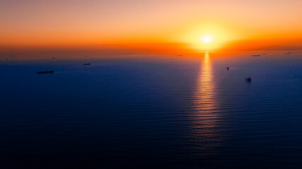 Orange sky with setting sun above the vast waterscape. Some ships are standing on the anchor....