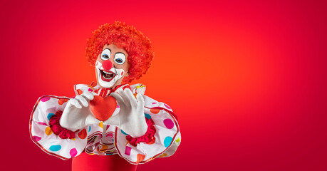 Funny clown with heart, man entertainer as Joker in a suit and wig, with clown whiteface makeup....