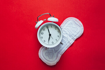 White alarm clock and menstrual sanitary pad on red background, flat lay.