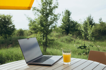 Glass of juice and laptop on the table on a blurred nature background.