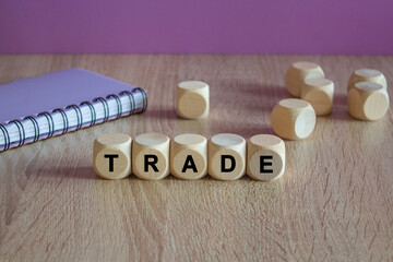 Trade symbol. Writing the word Trade on wooden cubes. Beautiful wooden table, purple background. Notebook. Business concept.