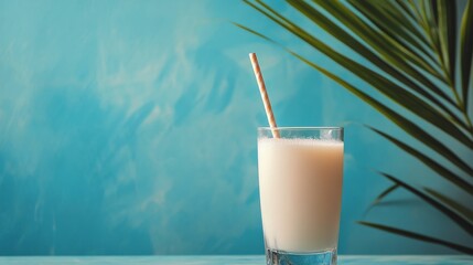 Refreshing beverage in a glass with straw surrounded by tropical leaves on vibrant blue background