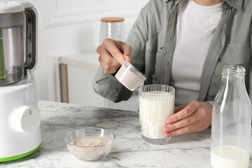 Making protein cocktail. Woman adding powder into glass with milk at white marble table, closeup