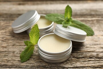 Natural lip balms and mint leaves on wooden background, selective focus