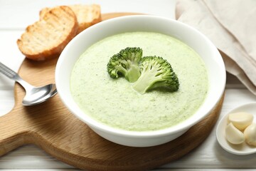Delicious broccoli cream soup served on white wooden table, closeup