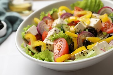 Delicious fresh Greek salad in bowl on white table, closeup