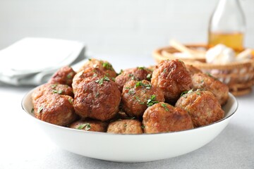 Tasty cooked meatballs with green onion in bowl on white table, closeup
