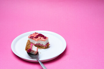 Layered cake with raspberries on a white plate, bright pink background creates contrast, a small piece on a spoon adds dynamics and sophistication.