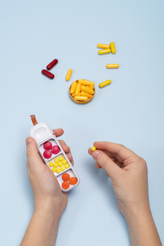 Top view of cropped unrecognizable hands organizing pills in a pillbox on blue background