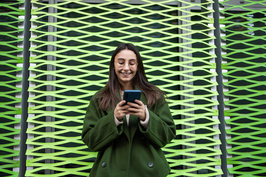 Woman in green coat smiling and using smartphone outdoors