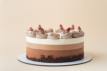 Homemade cake three chocolates on the beige background. Chocolate souffle cake with sponge cake and three layers of chocolate mousse decorated with whipped cream and dried flowers