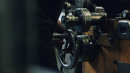 Metalworker operating an industrial lathe machine, turning a metal wheel and creating metal shavings, in a factory or workshop setting, showcasing the manufacturing process
