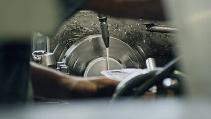 Metal processing within a factory, featuring a skilled worker operating a lathe machine while cooling a metal piece with oil, highlights the intricate industrial manufacturing process