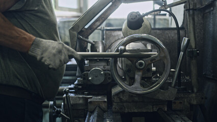Close up of a metalworker's hands operating a lathe, shaping a metal workpiece, showcasing the precision and skill involved in metal production