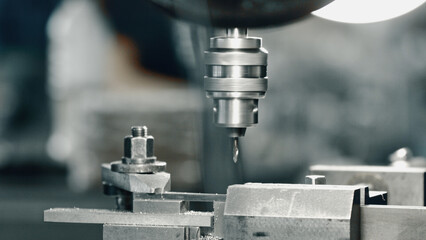 Close up view of an industrial drill press perforating a metal component in a factory, highlighting the precision and automation integral to the modern manufacturing process