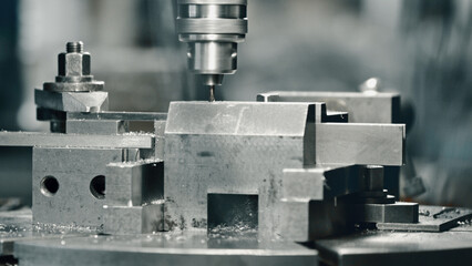 Close up of industrial drill press making precise hole in metal workpiece, showcasing manufacturing process with metal shavings and precision machinery