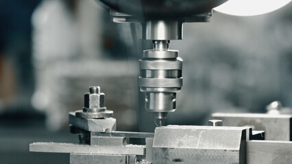 Industrial drill press rapidly perforating a metal component within a manufacturing facility,...