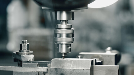 Close up of an industrial drill press actively working on a metal piece, showcasing the precision and power of modern manufacturing processes in a factory setting