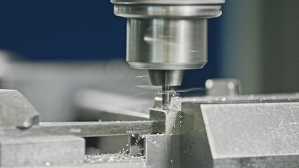 Automated milling machine is drilling a metal workpiece, creating small metal shavings, in a modern...