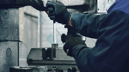 Close up of factory worker wearing gloves using a milling machine, producing metal parts in a...