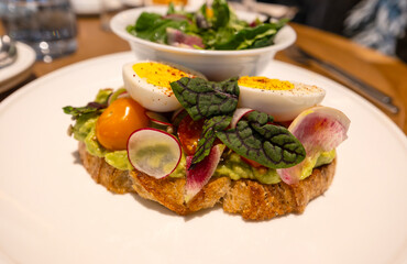 Close-up of Avocado Toast with Cherry Tomatoes, Raddishes, Turnips, Greens and Hard Boiled Egg Served with Herb Salad