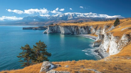 Scenic coastal landscape with white cliffs, turquoise water, and snow-capped mountains under a bright sky.