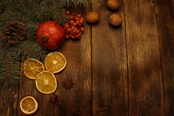 dark wooden background, fir branch in the left corner, dried oranges, red viburnum and star anise, nuts, pomegranate