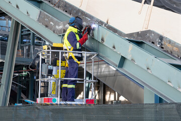 Welder working on aerial platform is welding metal structure