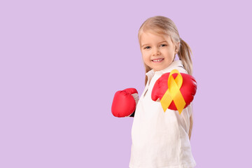 Cute little girl in boxing gloves with yellow ribbon on lilac background. Childhood cancer awareness concept