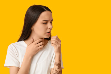 Beautiful young woman suffering from sore throat on yellow background