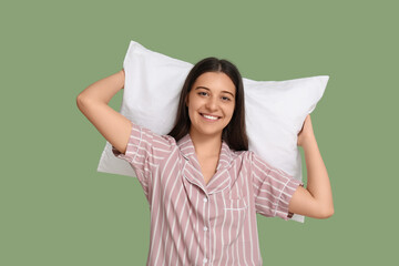 Young woman in pajamas with soft pillow on green background