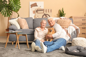 Happy senior couple with cute Pomeranian dog sitting on floor at home