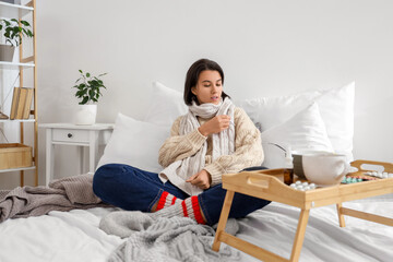 Sick young woman measuring temperature in bedroom